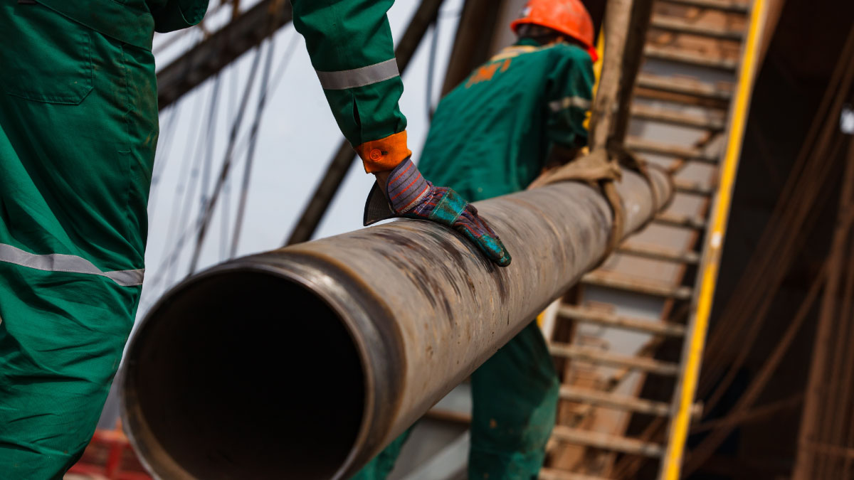 Two oil workers in green and orange work wear and suede gloves with rusted drilling pipe at an oil deposit in Kazakhstan.